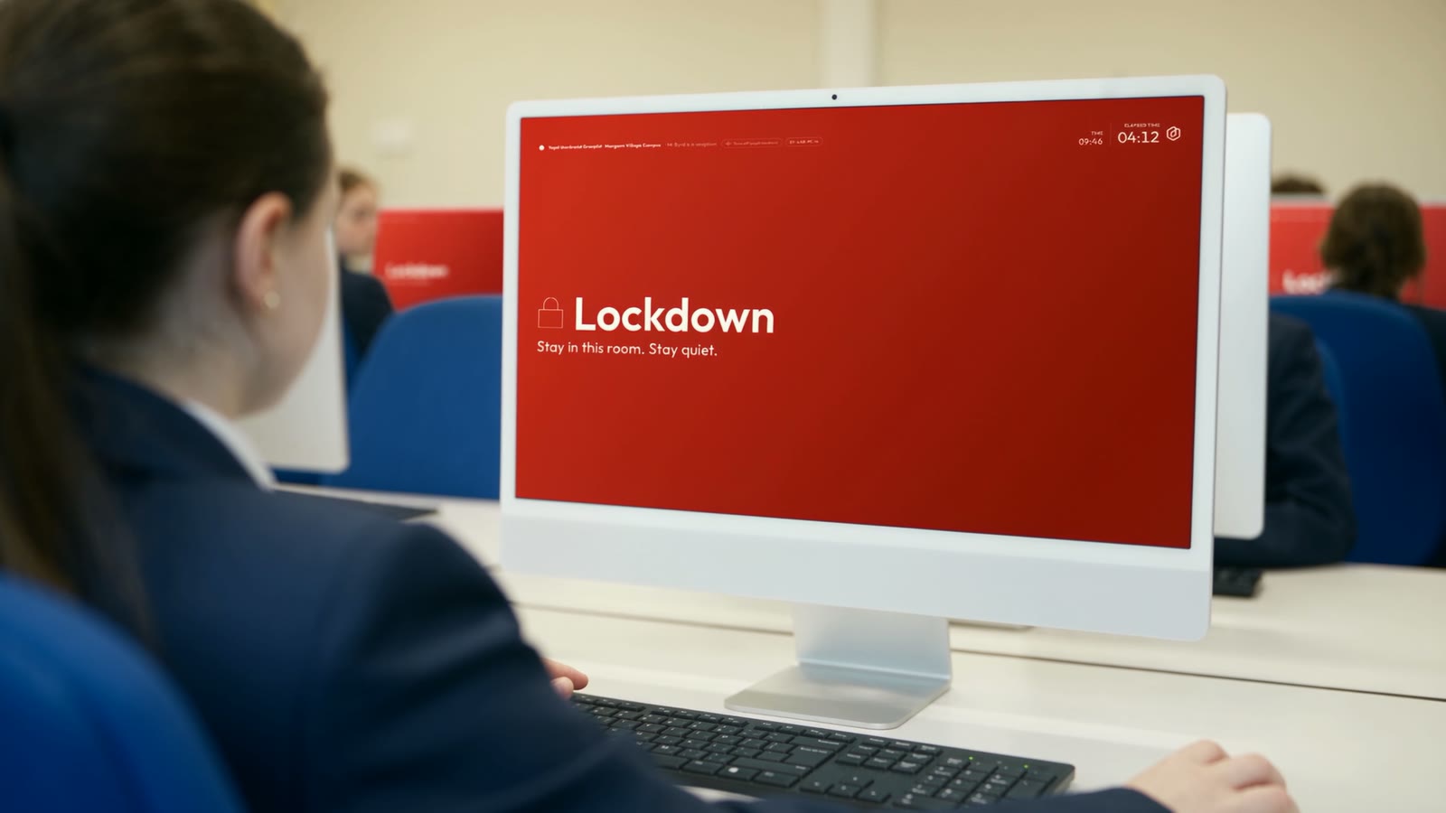 A pupil at a classroom iMac, its screen filled with the red lockdown message: stay in this room, stay quiet
